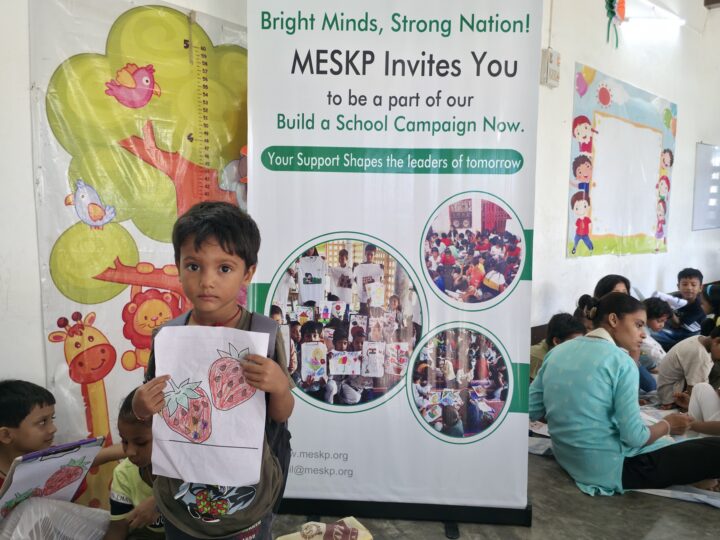 Boy holding his drawing in front of the Build a School campaign banner