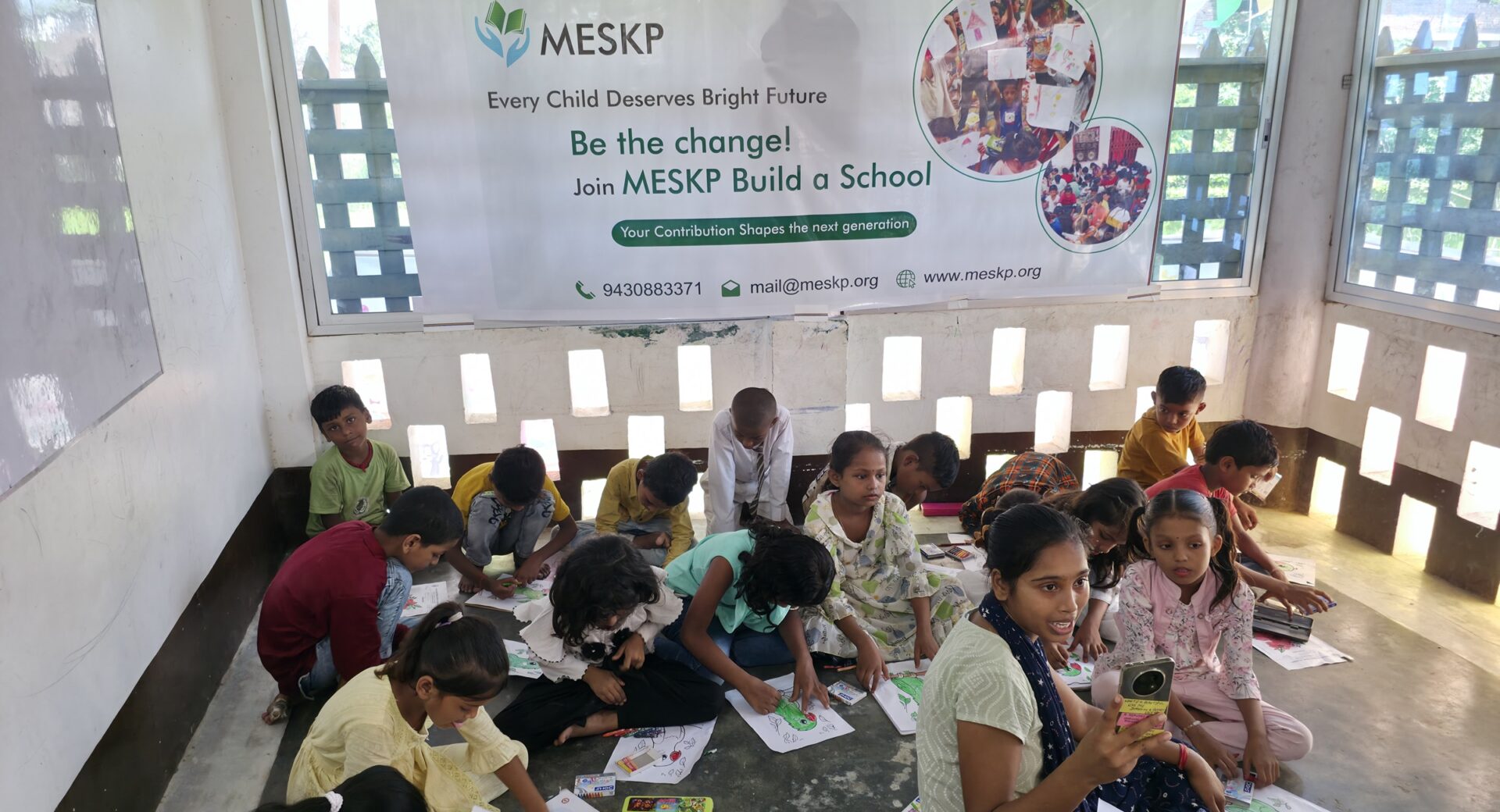 Children drawing under the Build a School banner